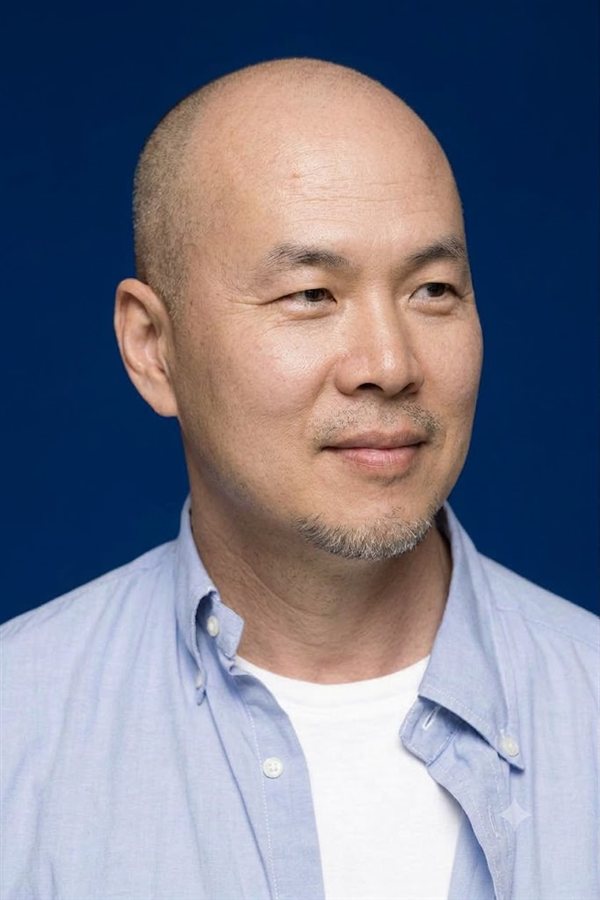 Gen 캐릭터 이미지: 짙은 남색 배경 앞에서 하늘색 셔츠를 입고 옅게 미소 짓는 민머리의 남성